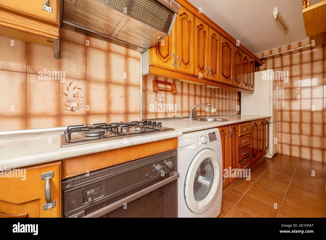Kitchen with cream-colored imitation marble wood countertops and orange-brown tiles with rustic wood cabinets and integrated appliances Stock Photo