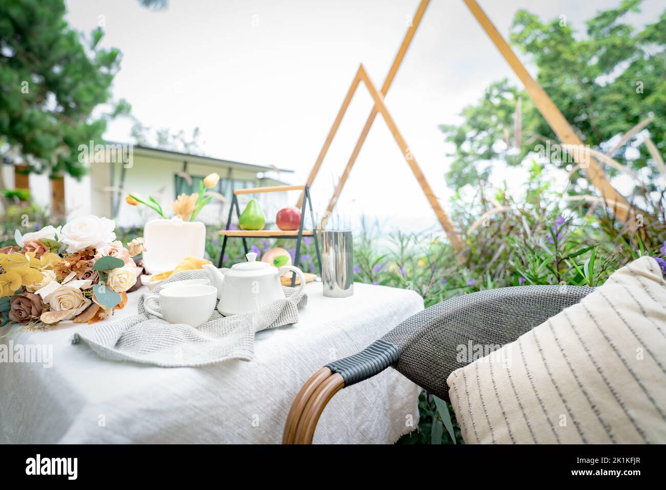 Coffee cup and flowers bouquet on table in garden. Afternoon tea concept. Home outdoor furniture. Wicker chair and table with white tablecloth Stock Photo