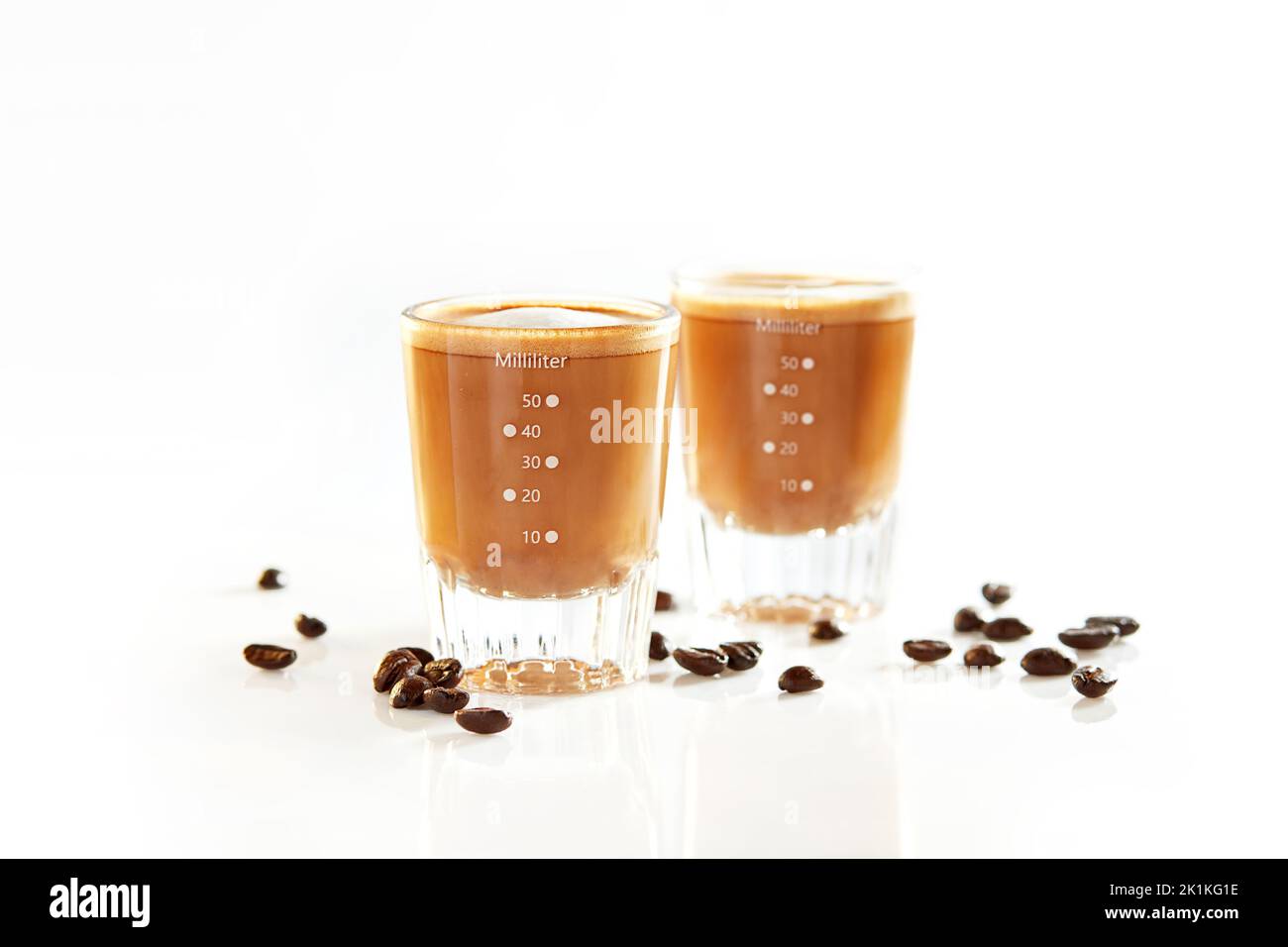 Two shots of coffee with milk and roasted coffee beans on a table Stock