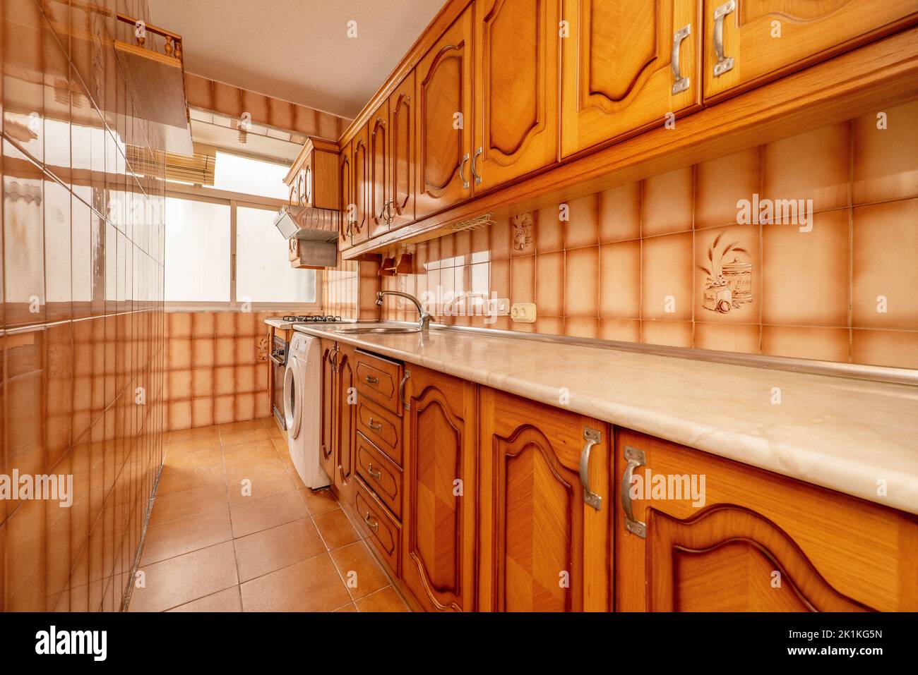 https://c8.alamy.com/comp/2K1KG5N/long-kitchen-with-cream-marble-look-wood-countertops-and-orange-brown-tiles-with-rustic-wood-cabinets-rear-window-and-built-in-appliances-2K1KG5N.jpg