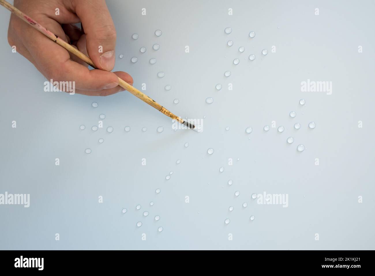 Male hand with a drawing brush draws a snowflake from water drops, on a gray background. Flat lay. Top view.  Stock Photo