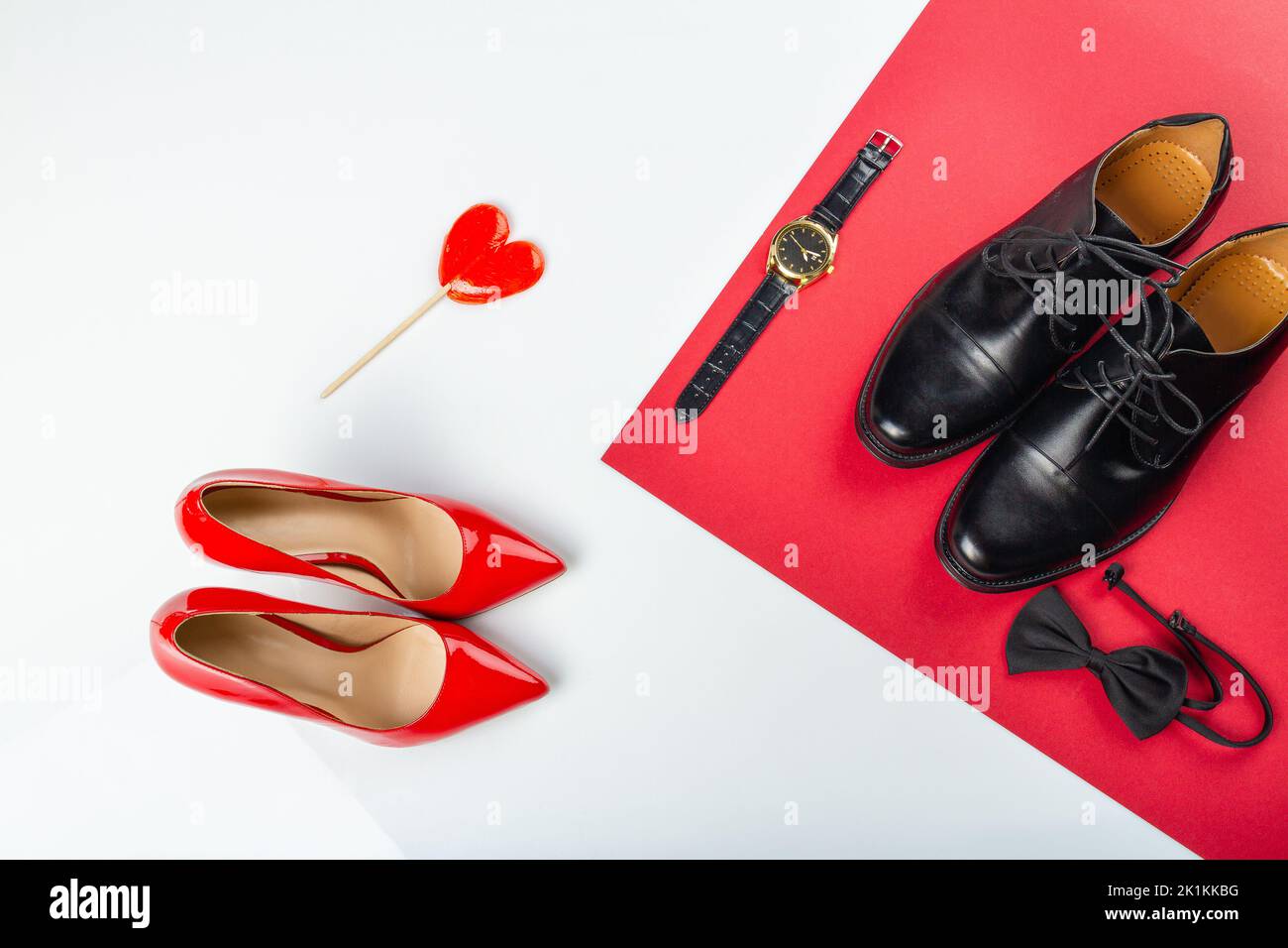 Top view mens and womens shoes on white background. Red and black shoes with lollipop and hand watch. Stock Photo
