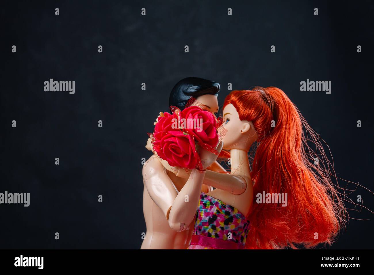 Kissing man and woman doll with red flowers. Loving couple on black background. Stock Photo