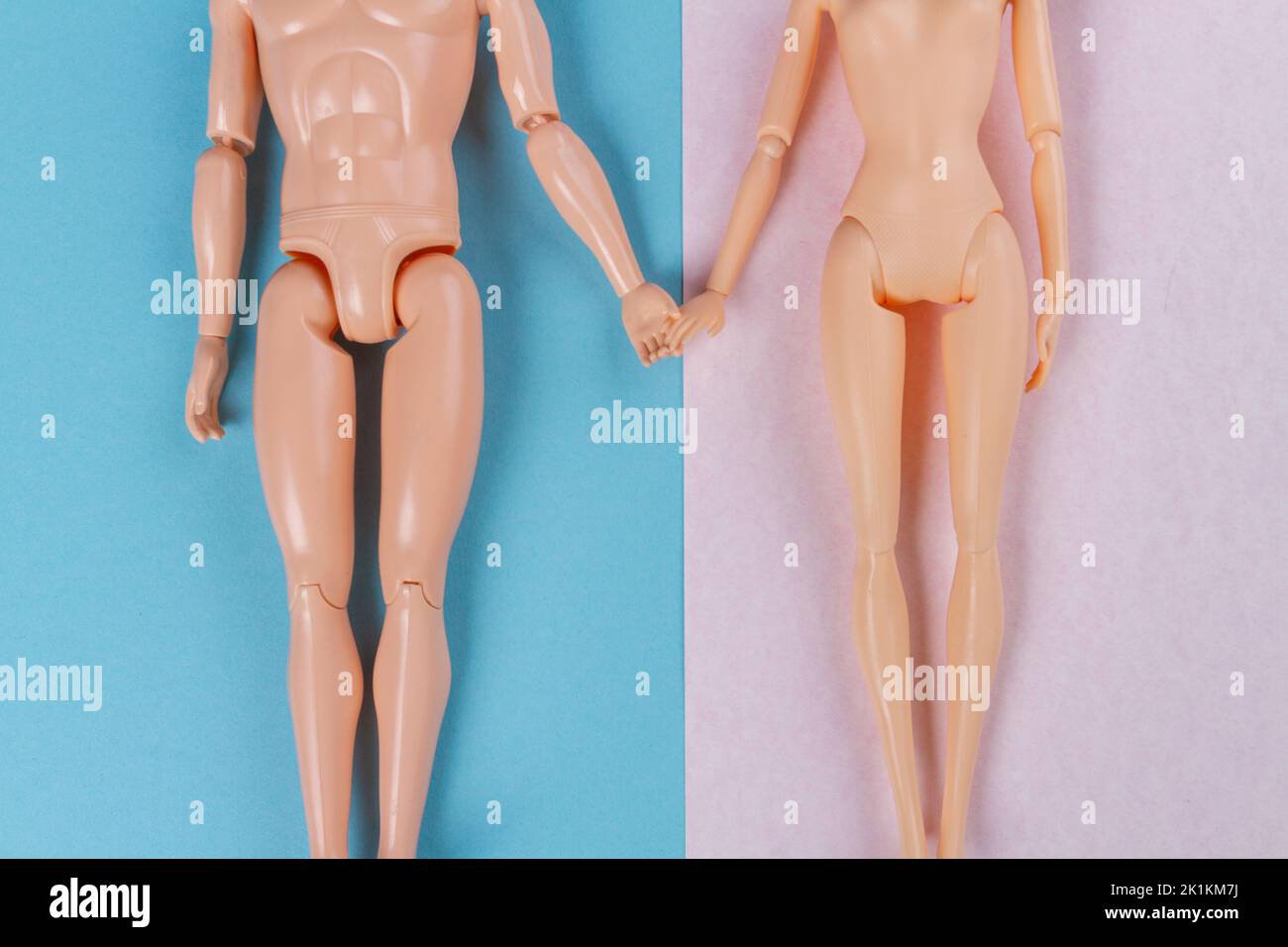 Top view naked doll couple holding hands. Blue and pink background. Stock Photo