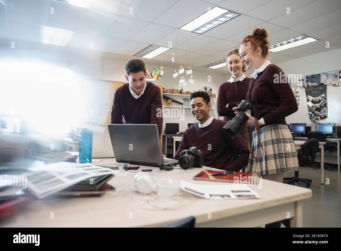 High school students with SLR cameras working on yearbook in classroom