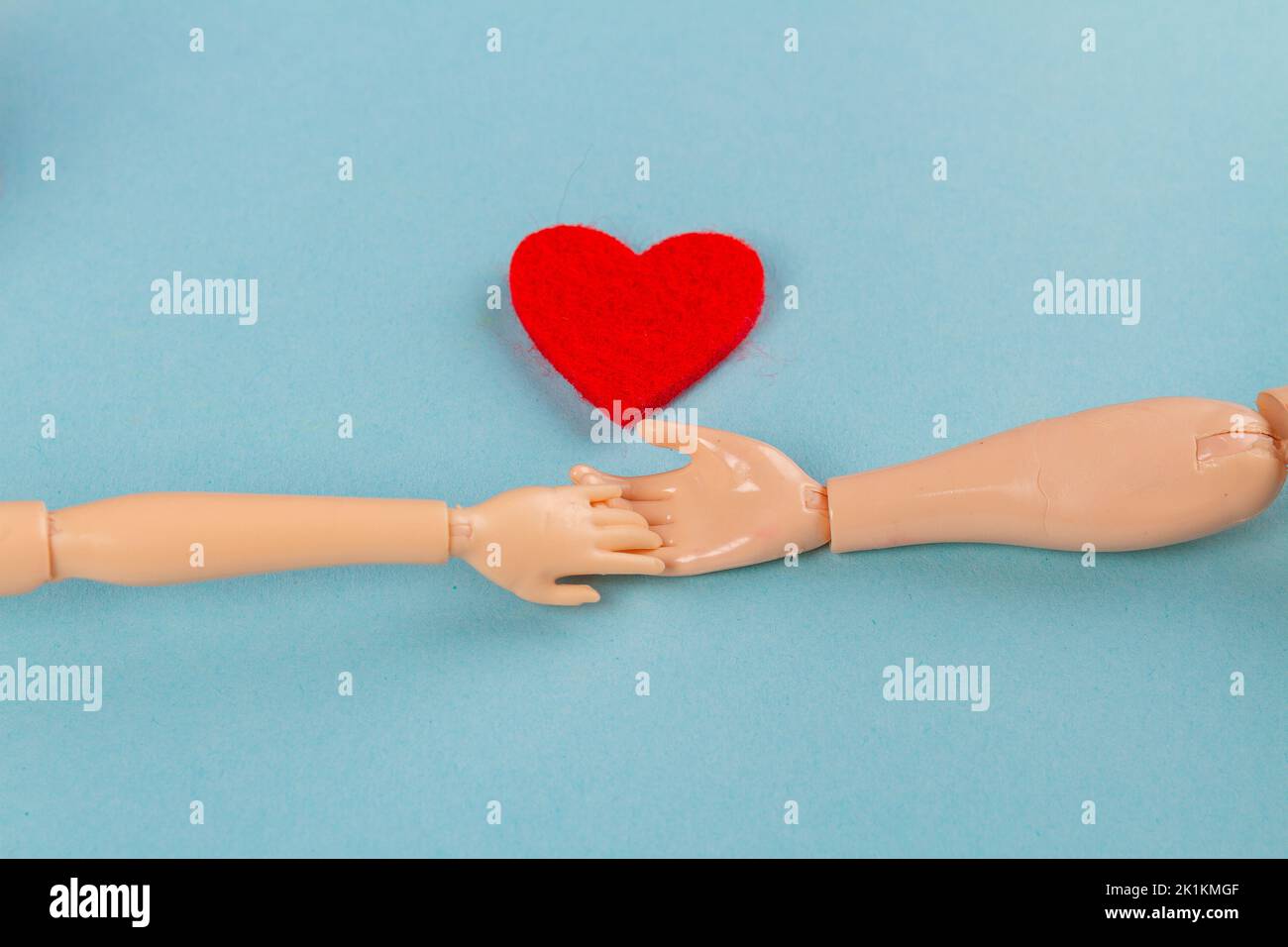 Doll hands holding and red heart on blue background. Love or charity concept. Stock Photo
