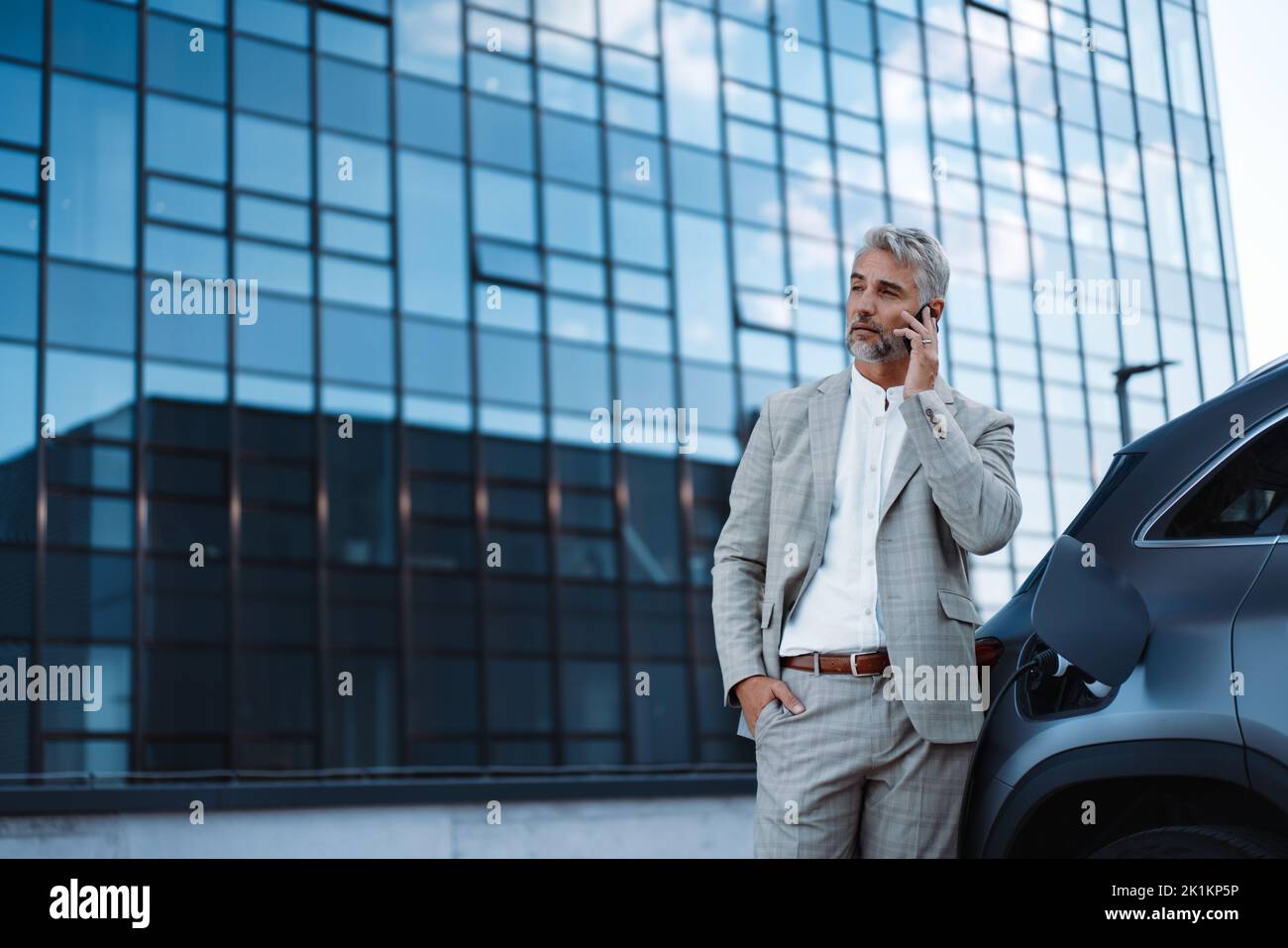 Businessman holding smartphone while charging car at electric vehicle charging station, closeup. Stock Photo