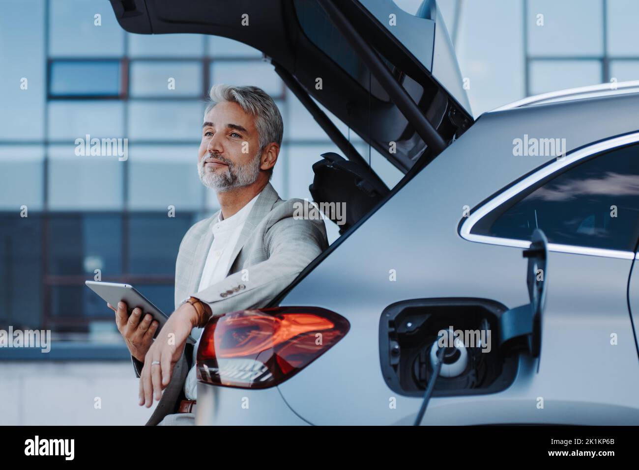 Businessman using tablet while charging car at electric vehicle charging  station, close-up Stock Photo - Alamy