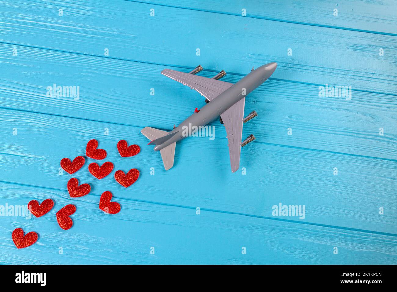 Top view of toy passenger boeing plane with red hearts. Blue wooden desk surface. Stock Photo