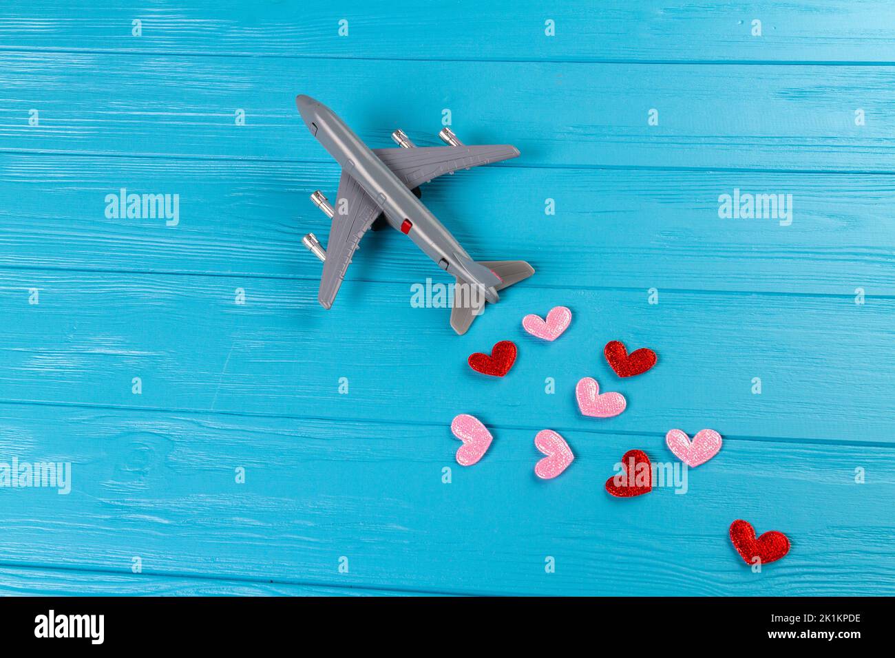Toy passenger plane with hearts on a blue background. Top view flat lay. Distribution of love concept. Stock Photo