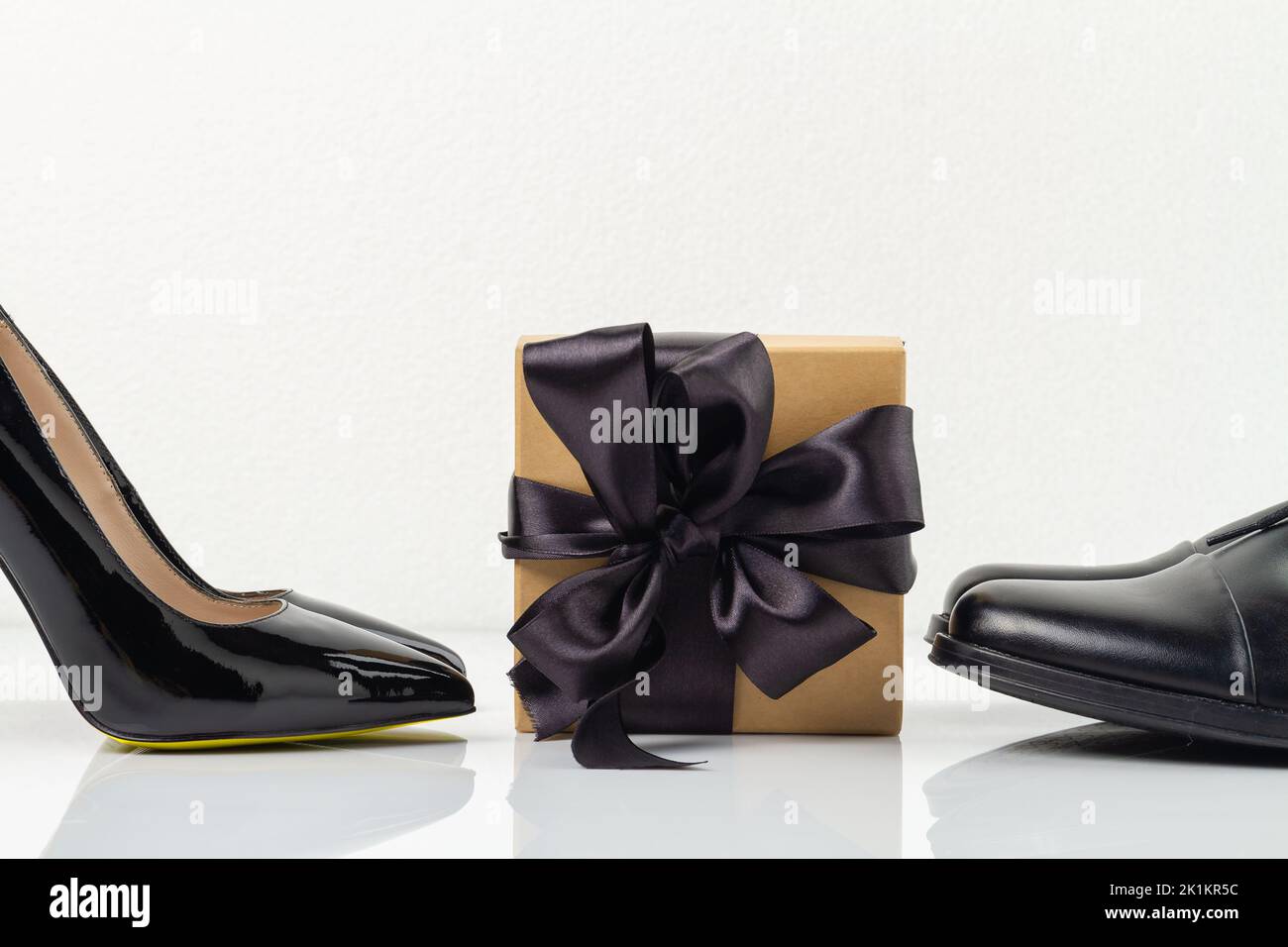 Still life of gift box with black ribbon and shoes. Classic black mens and womens footwear isolated on white. Stock Photo