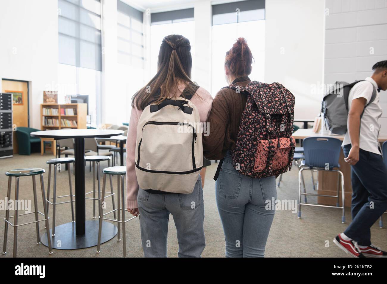 High school girl students with backpacks walking in library Stock Photo