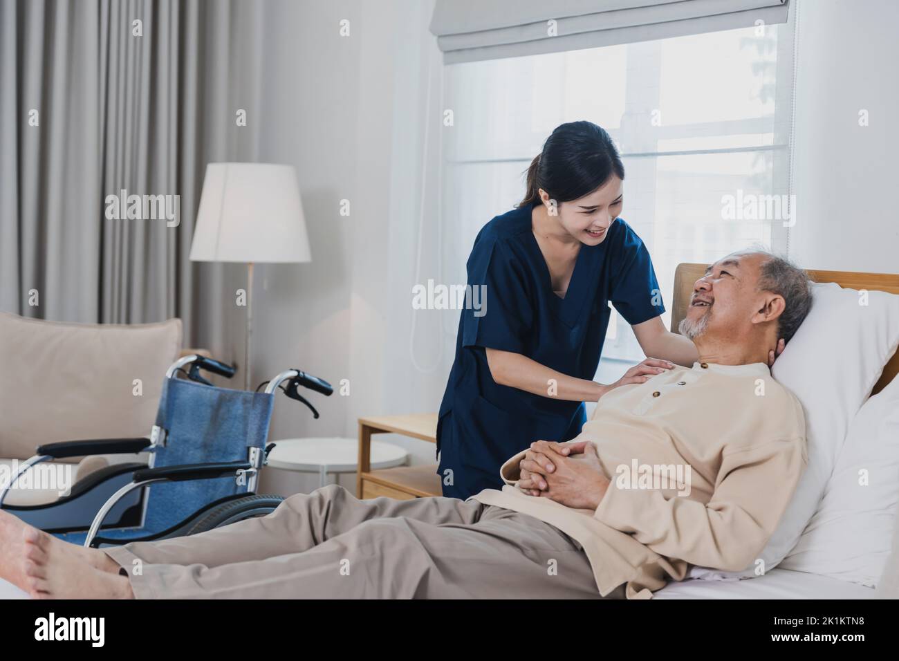 Senior Asian man laying on bed receives medical help for injury by Asian nurse, doctor woman assisting Stock Photo