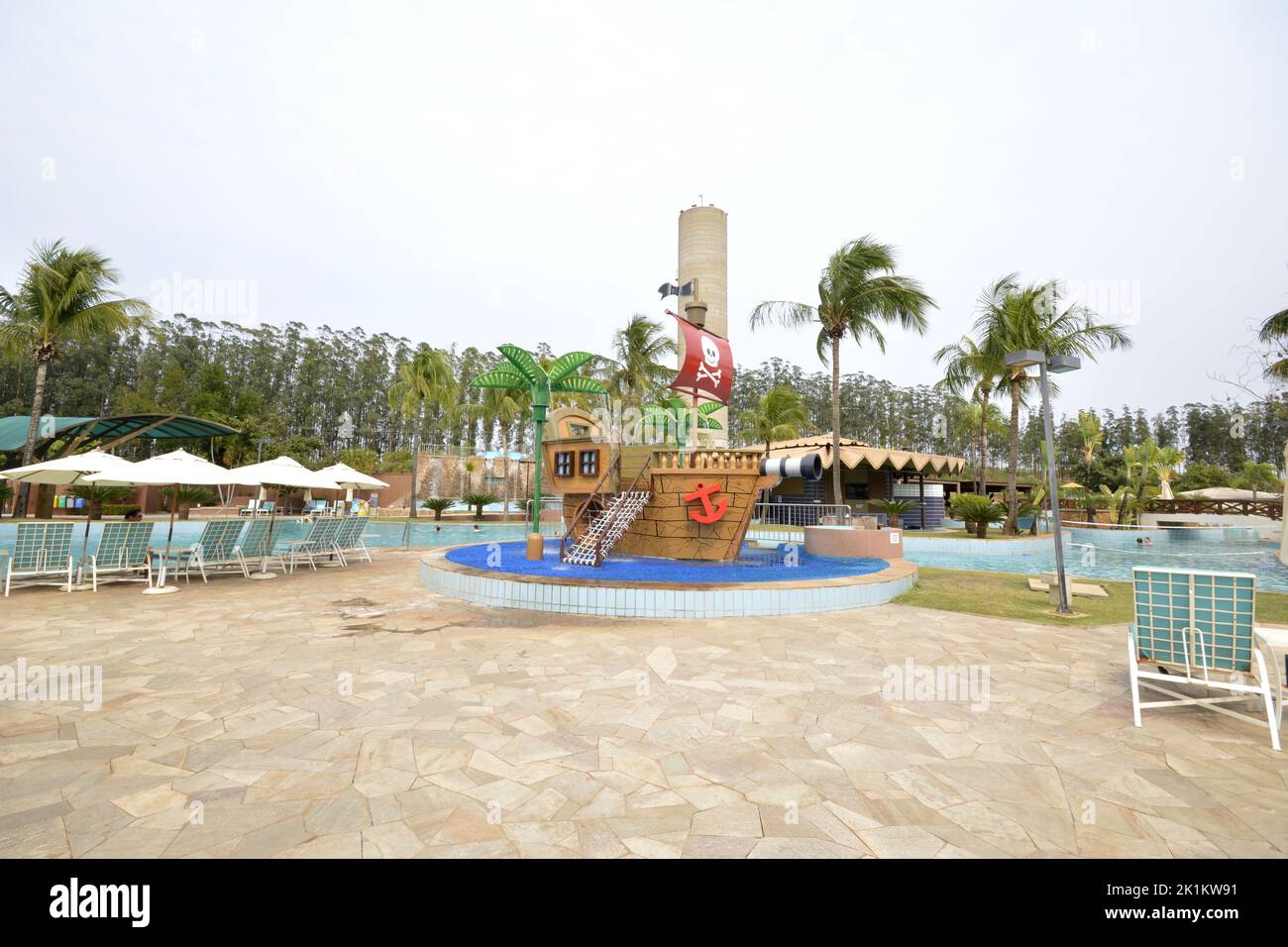 Tourists at a luxury resort pool with waterfall and sun loungers in the background on a blue cloudy day. panoramic. Foreground pirate ship for kids Stock Photo