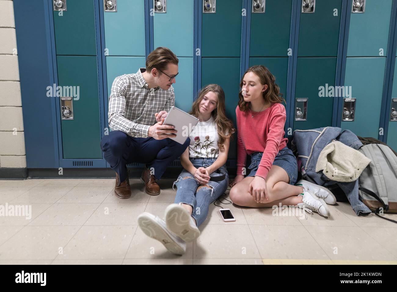 High school teacher with digital tablet talking to students at lockers ...