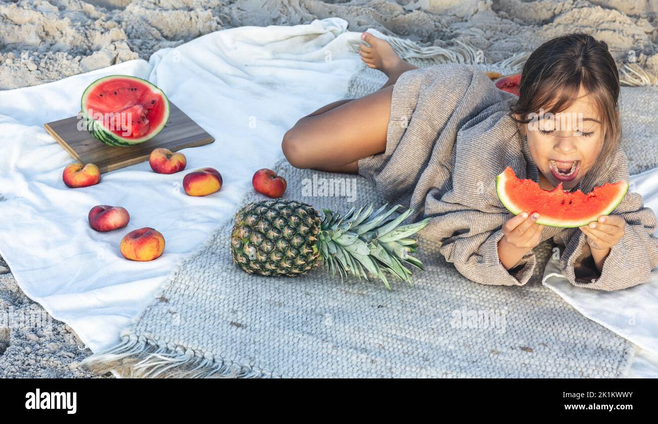 Little girl eats fruit lying on a blanket on the beach Stock Photo Alamy