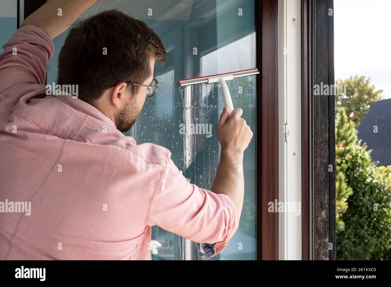 Man opened the window sash and washes the glass from dust and dirt using a special scraper tool. Cleaning. Stock Photo