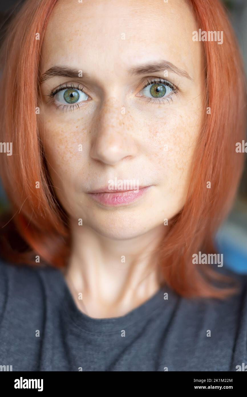 Young pretty woman with red hair, green eyes and freckles looks carefully at the camera. Close-up, selective focus. Stock Photo