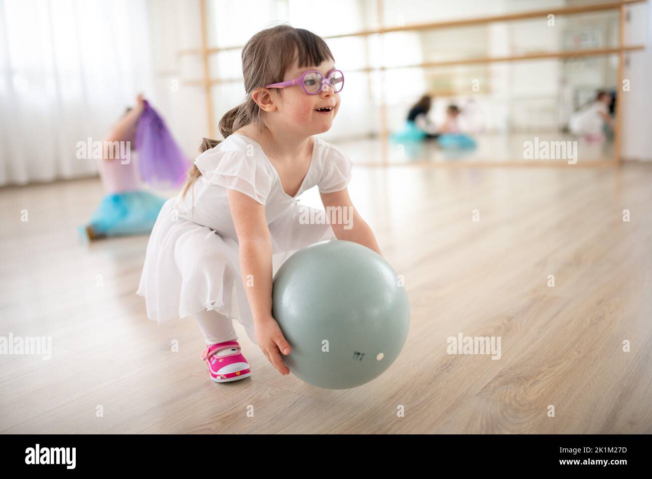 Little girl with down syndrome playing with ball at ballet class in