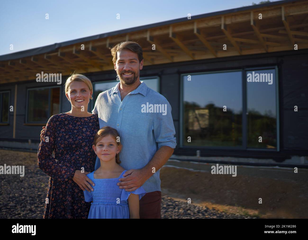 Young family standing in front of their new ecologic wooden house, concept of sustainability and healthy living. Stock Photo