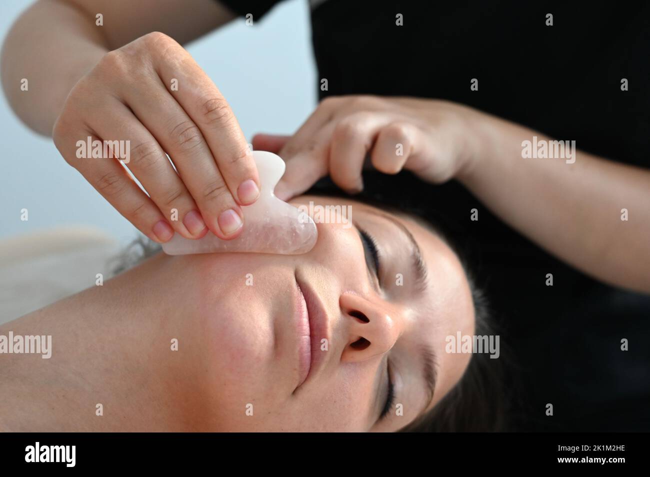 Cosmetologist does a facial massage with a gouache scraper. close up. Professional anti-aging facial massage.  Stock Photo