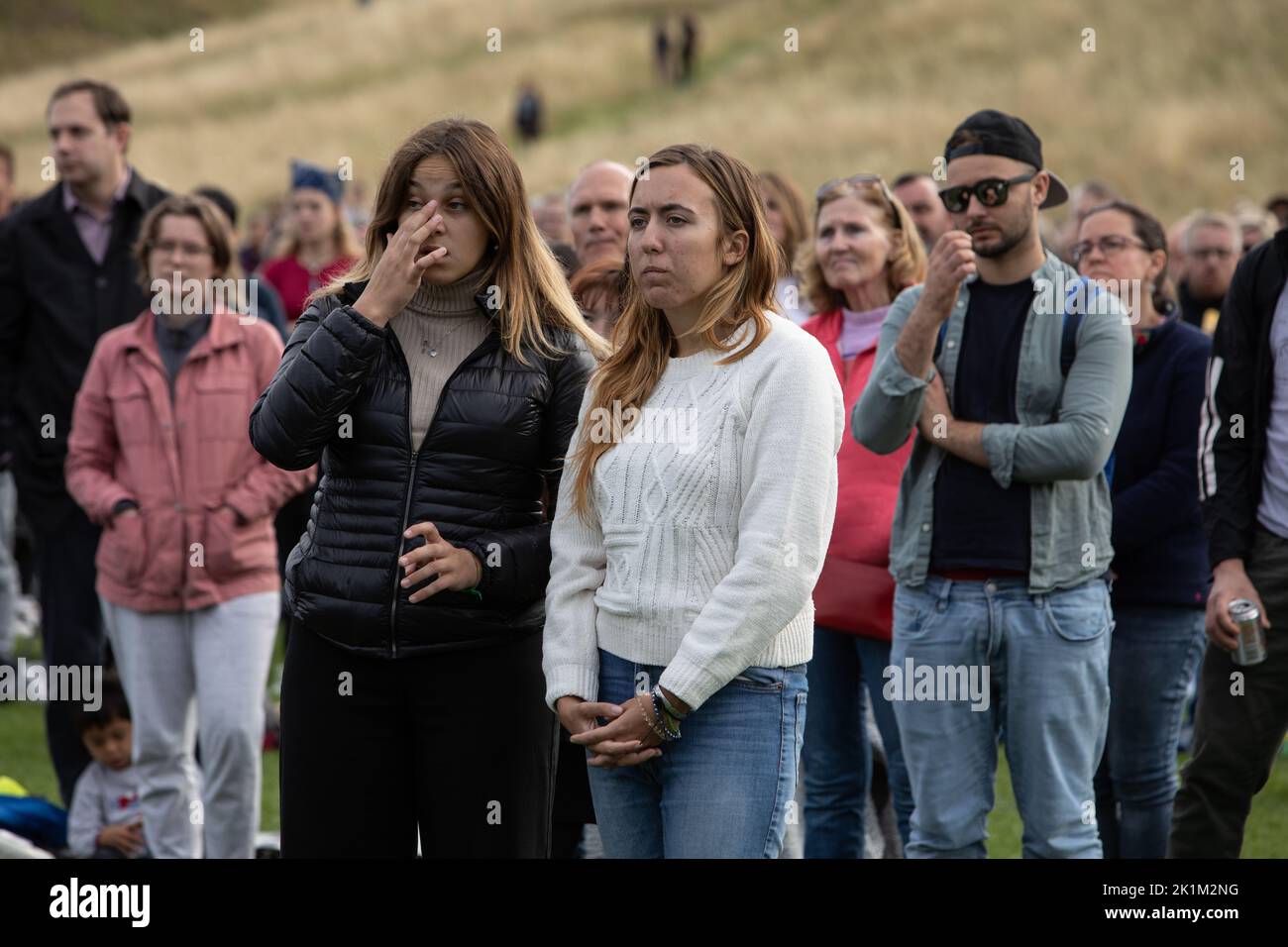 Edinburgh Scotland, 19 September 2022. In Holyrood Park, in front of the Royal family’s Palace of Holyroodhouse, crowds stand for 2-minutes silence as they watch on a large screen the funeral in London of Her Majesty Queen Elizabeth II who died on 8th September, in Edinburgh Scotland, 19 September 2022. Photo credit: Jeremy Sutton-Hibbert/Alamy Live News. Stock Photo