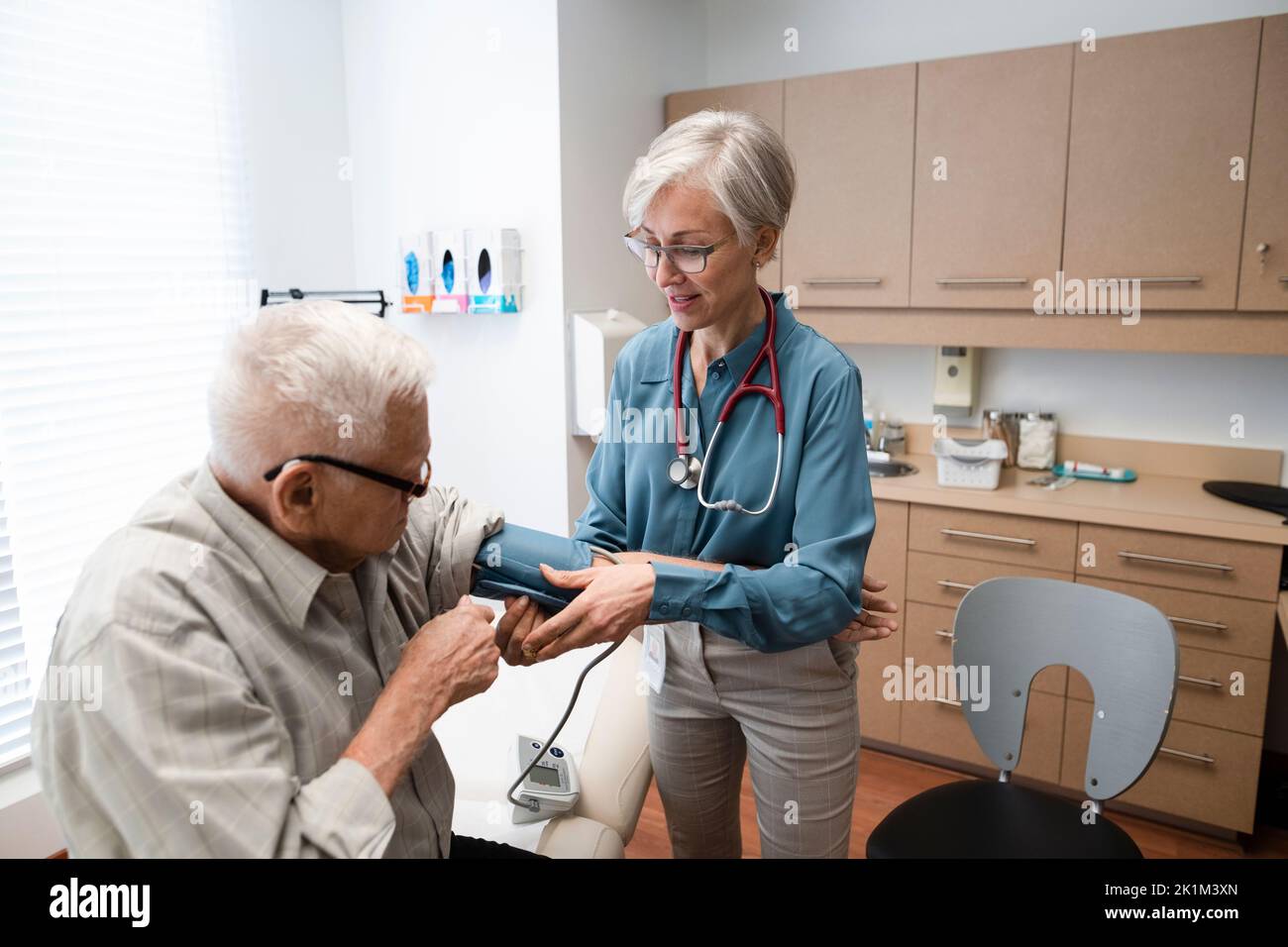 Doctor checking blood pressure of senior patient in clinic exam room Stock Photo