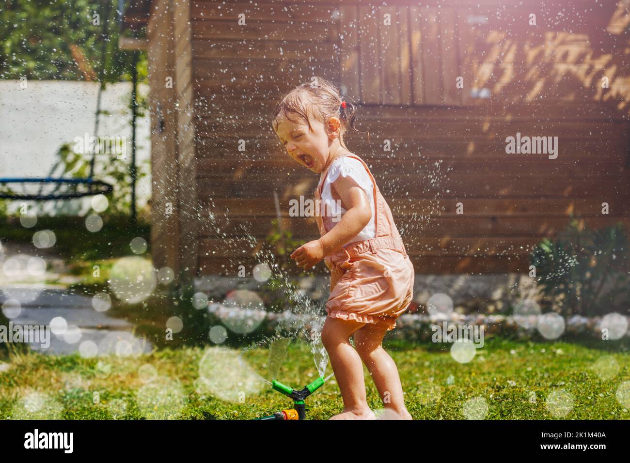Beautiful girl in wet clothes play with sprinkler at garden Stock Photo