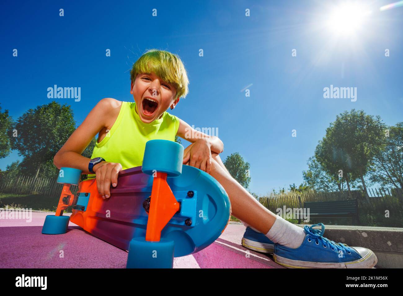 Happy screaming boy with skateboard and green hair sit on a ramp Stock Photo