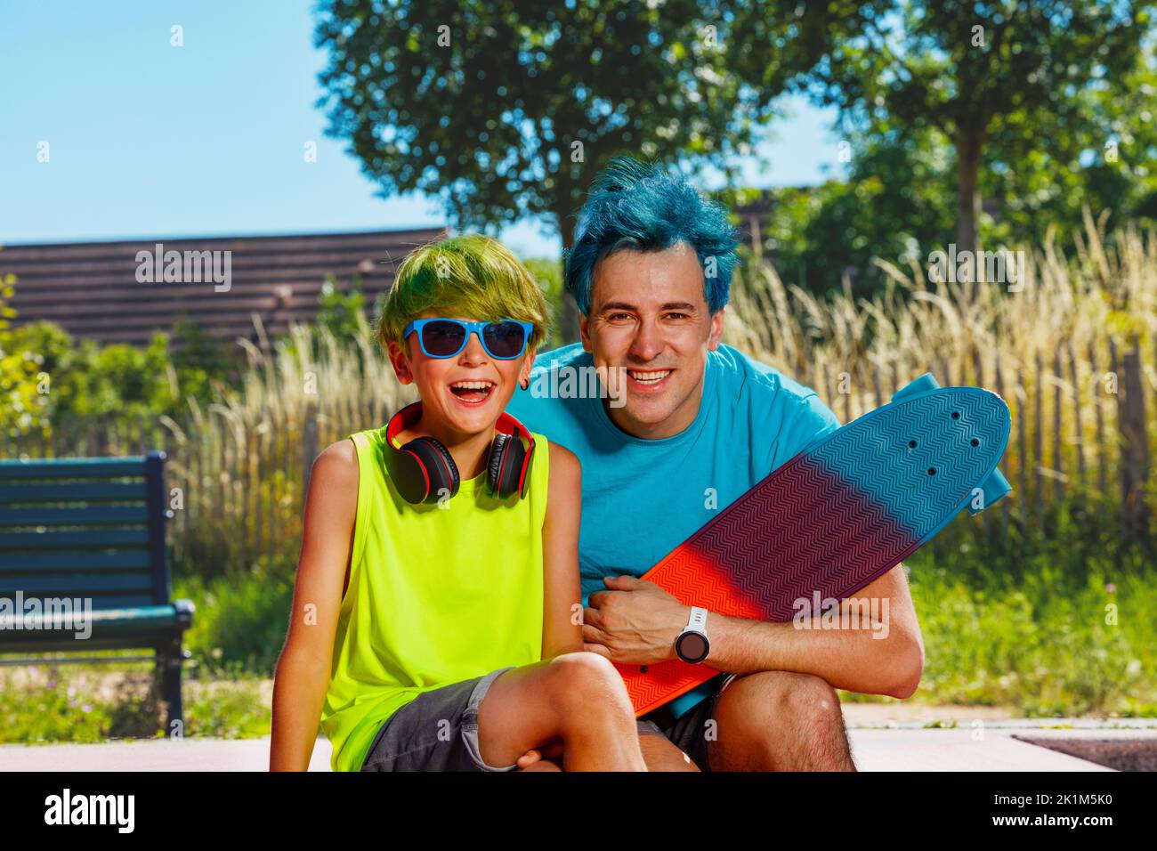 Father with color hair sit by son holding skateboard and smile Stock Photo