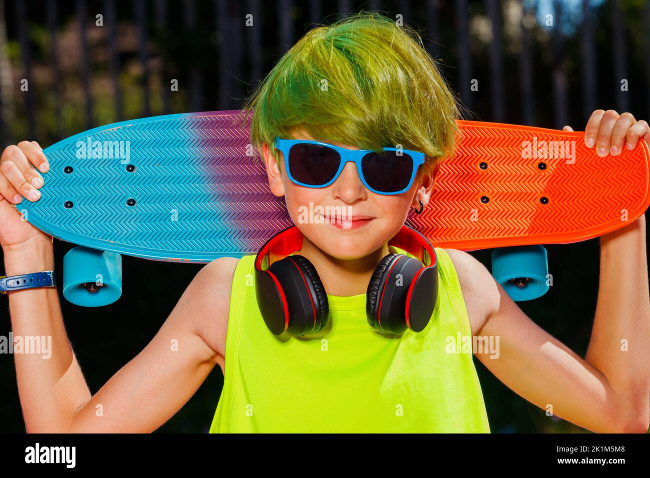 Close-up portrait of a boy with skateboard green hair headphones Stock Photo