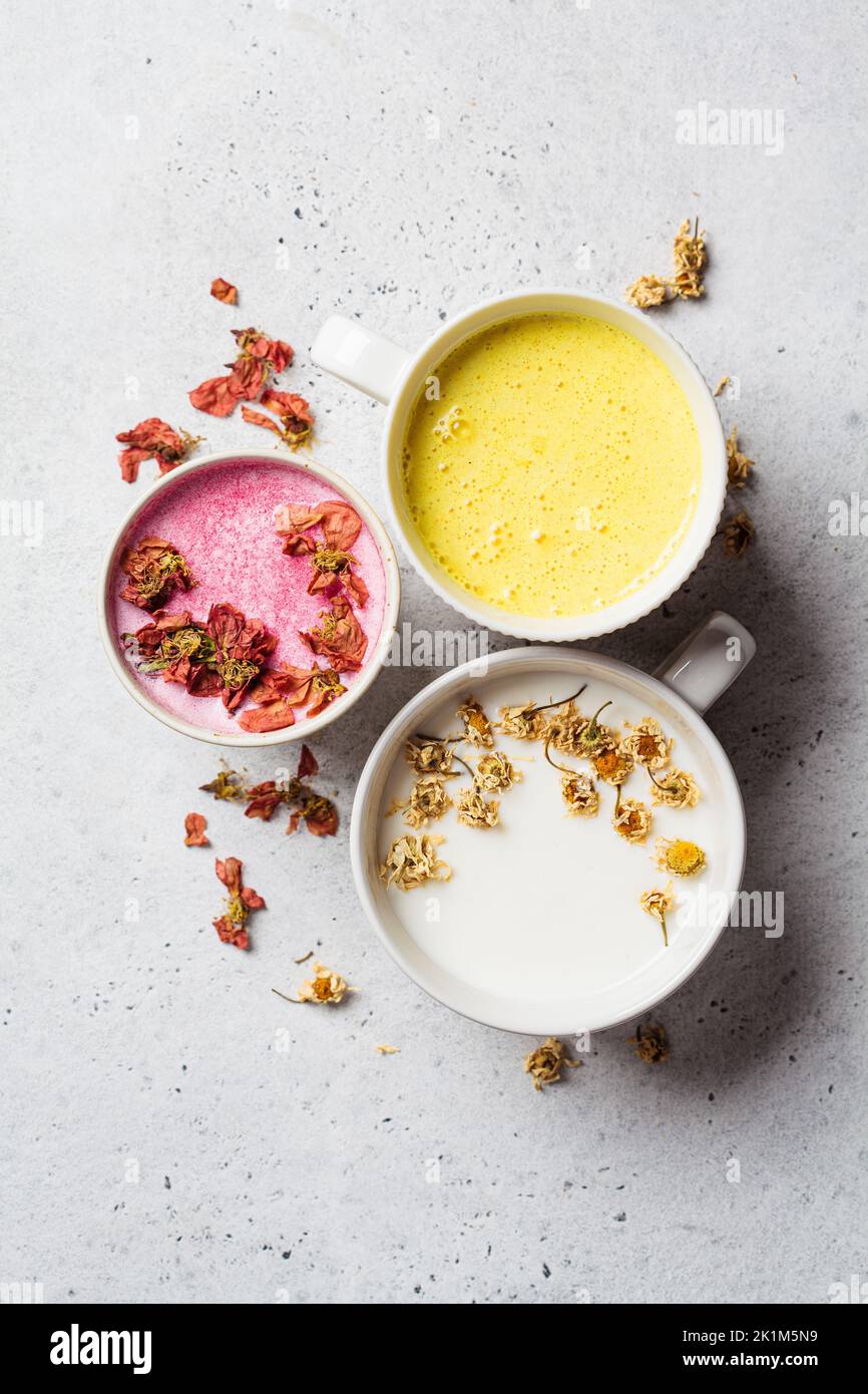 Different types of moon milk: rose flower, golden turmeric and chamomile in white cups, top view. Ayurveda drink, healthy lifestyle, remedy for insomn Stock Photo