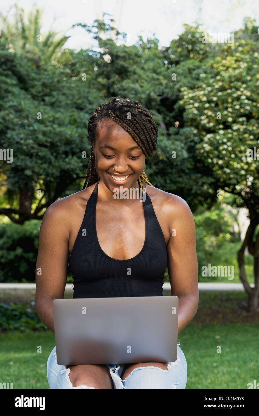 Young African American woman sitting on a bench, using a laptop computer.  Stock Photo