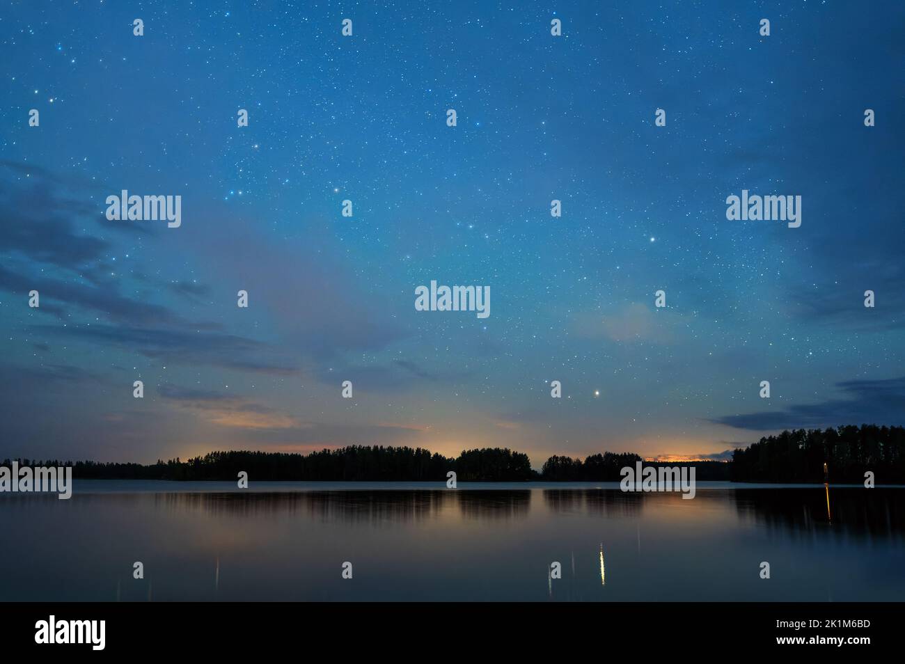 Night landscape under starry sky, stars reflecting from calm water surface, distant thunder in the horizon. Stock Photo