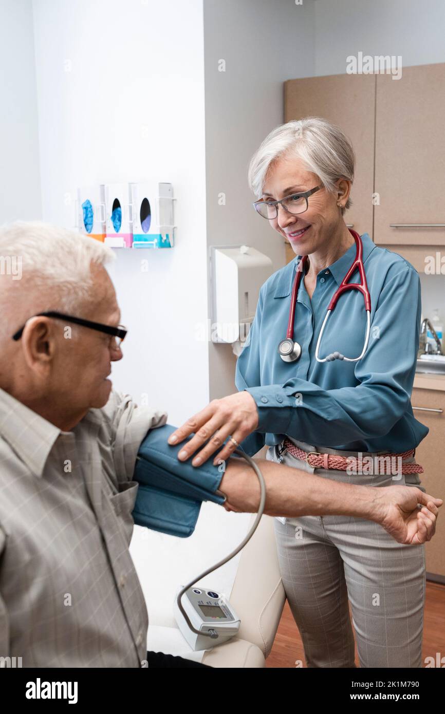 Senior doctor checking blood pressure of patient in clinic exam room Stock Photo