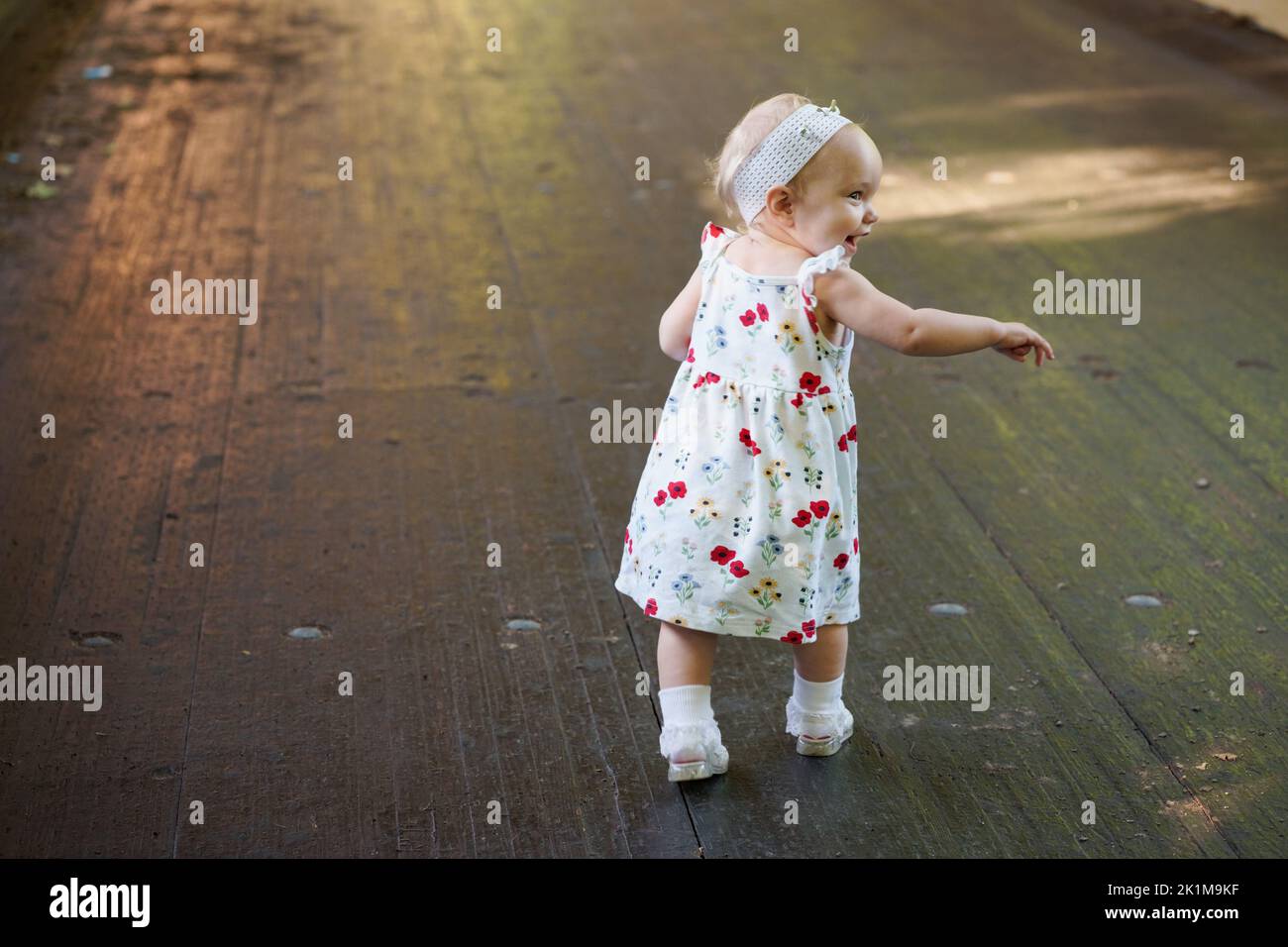 A rear view of a baby girl in a white dress with red roses running on a ...