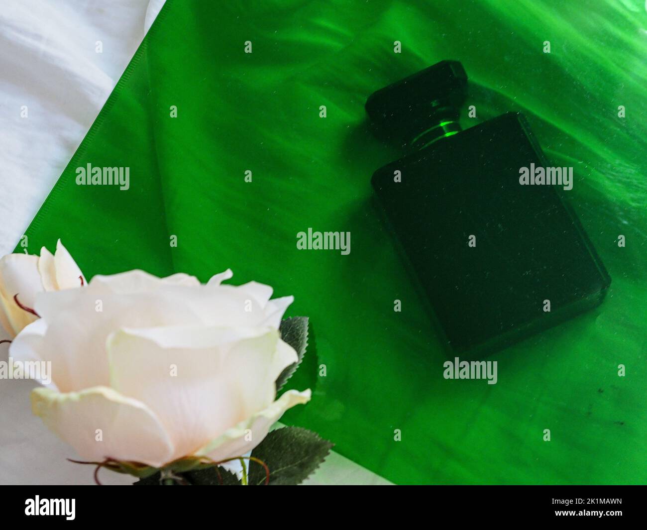 A top view of a black perfume bottle on bed sheets with a white rose