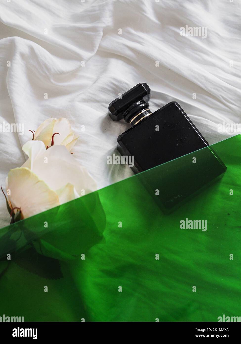 A vertical shot of a black perfume bottle on bed sheets with a white