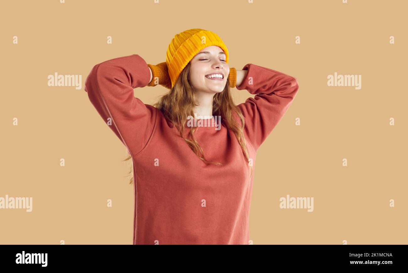 Relaxed woman in autumn clothes puts hands behind head, closes eyes, breathes in air and smiles Stock Photo