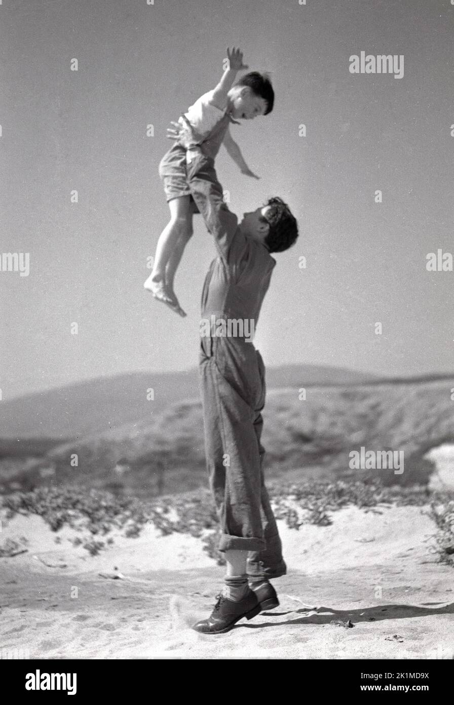 1930s, historical, man in overalls, car mechanic, holding up his young son on sandy ground, Utah, USA. Stock Photo
