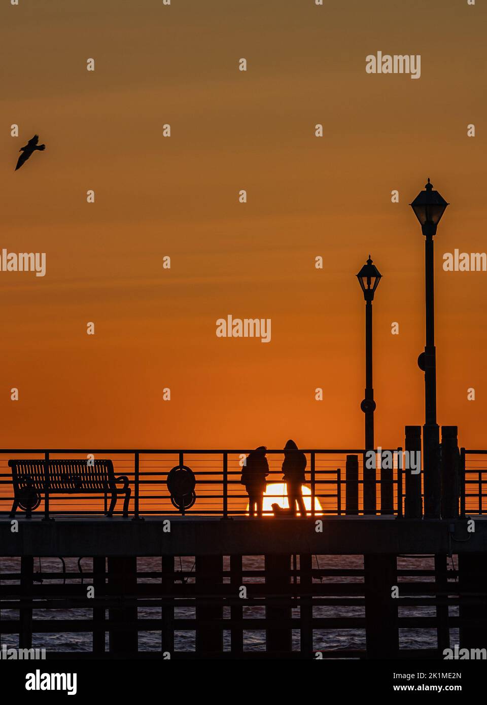 A silhouette of people on a bridge over sea during sunset, vertical ...