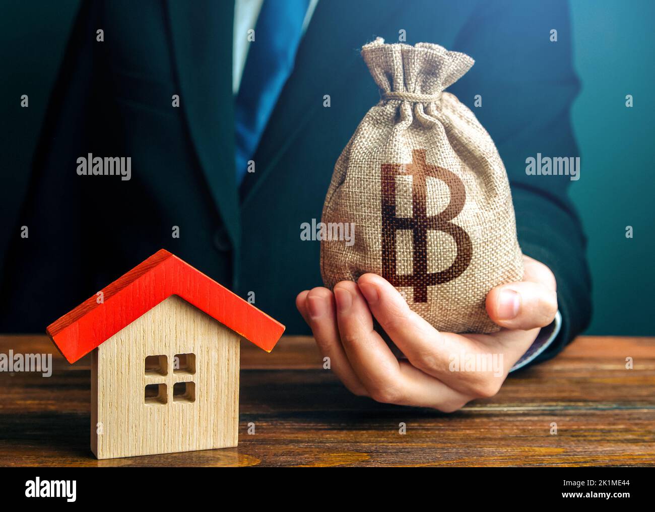 Man holds out a thai baht bag near the house. Bank approval for issuing a mortgage loan. Property appraisal. Home purchase, invest in real estate. Fav Stock Photo