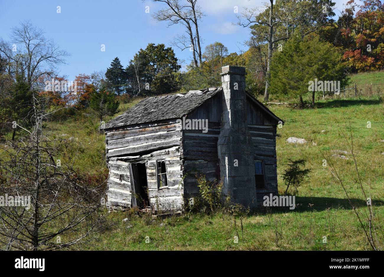 Old log cabin with wood shingle roof, lays abandoned on a hillside in the Appalachian Mountains.  Door hangs open. Stock Photo