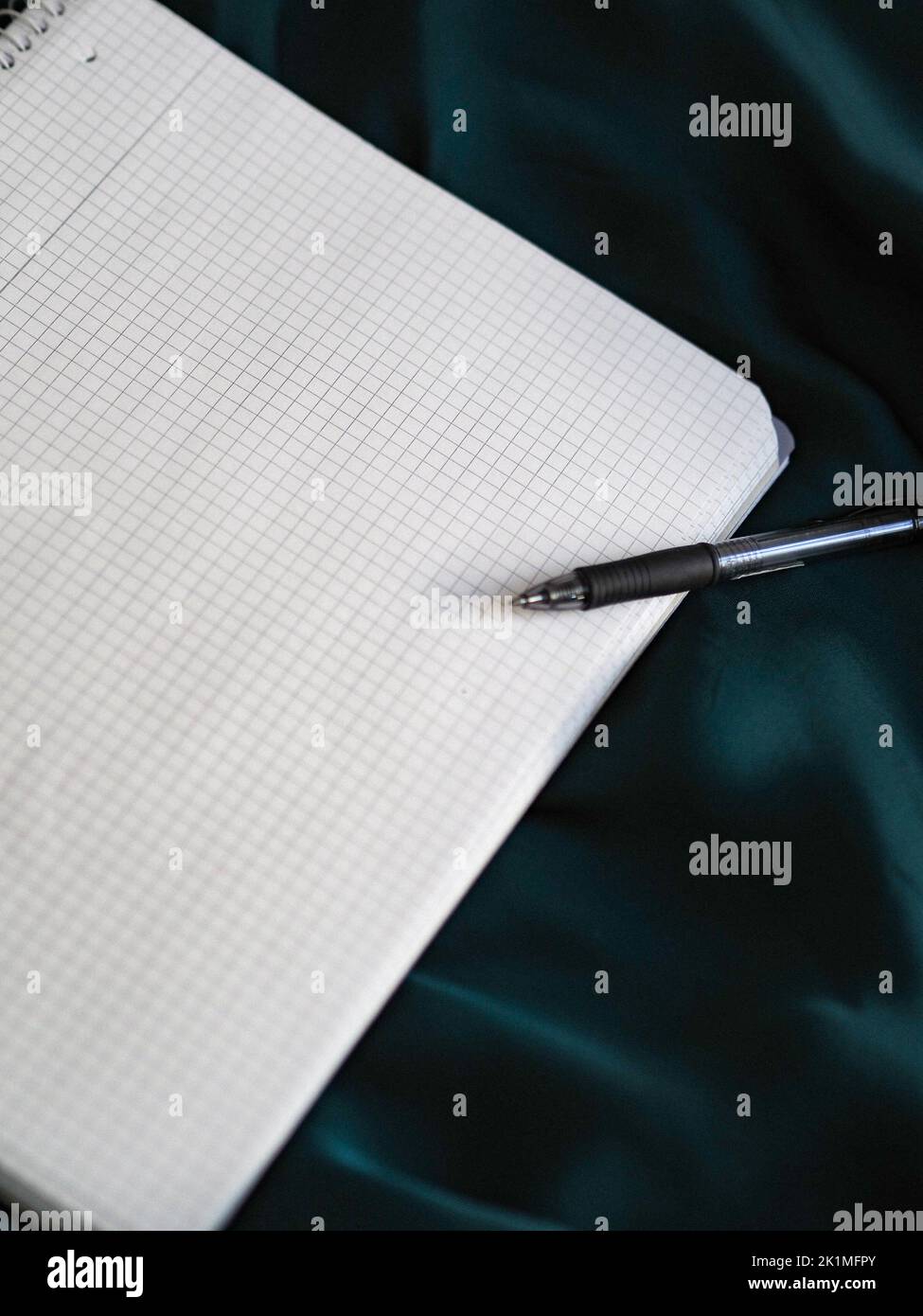 A pen and graphing paper on a shiny blue fabric surface, vertical shot Stock Photo