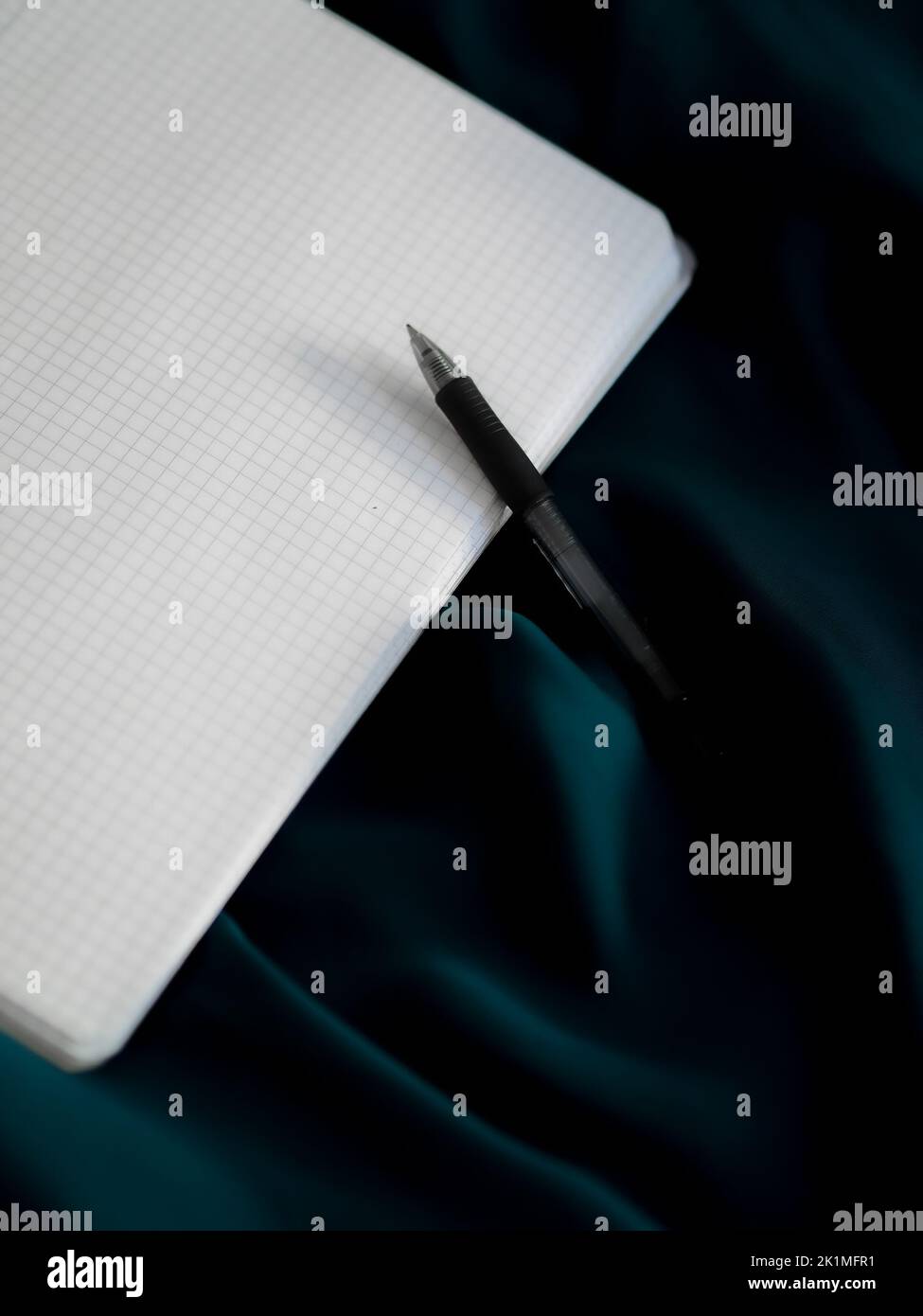 A pen and graphing paper on a shiny blue fabric surface Stock Photo