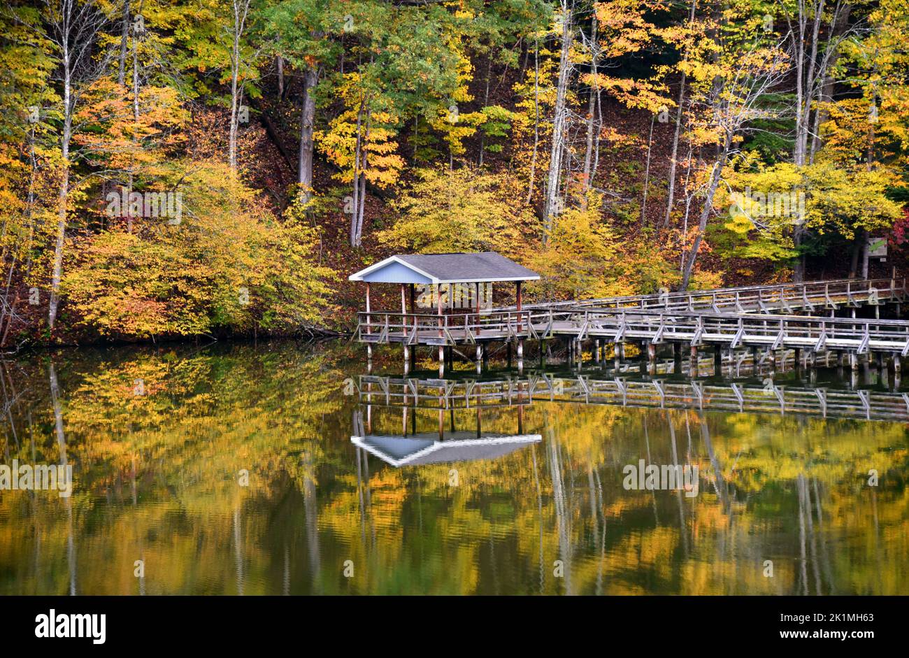 Wooden pavilion, over Steele Creek Lake in Bristol, Tennessee, is reflected on the calm water on an Autumn Day.  Walkway leads to Slagle Hollow Knob. Stock Photo