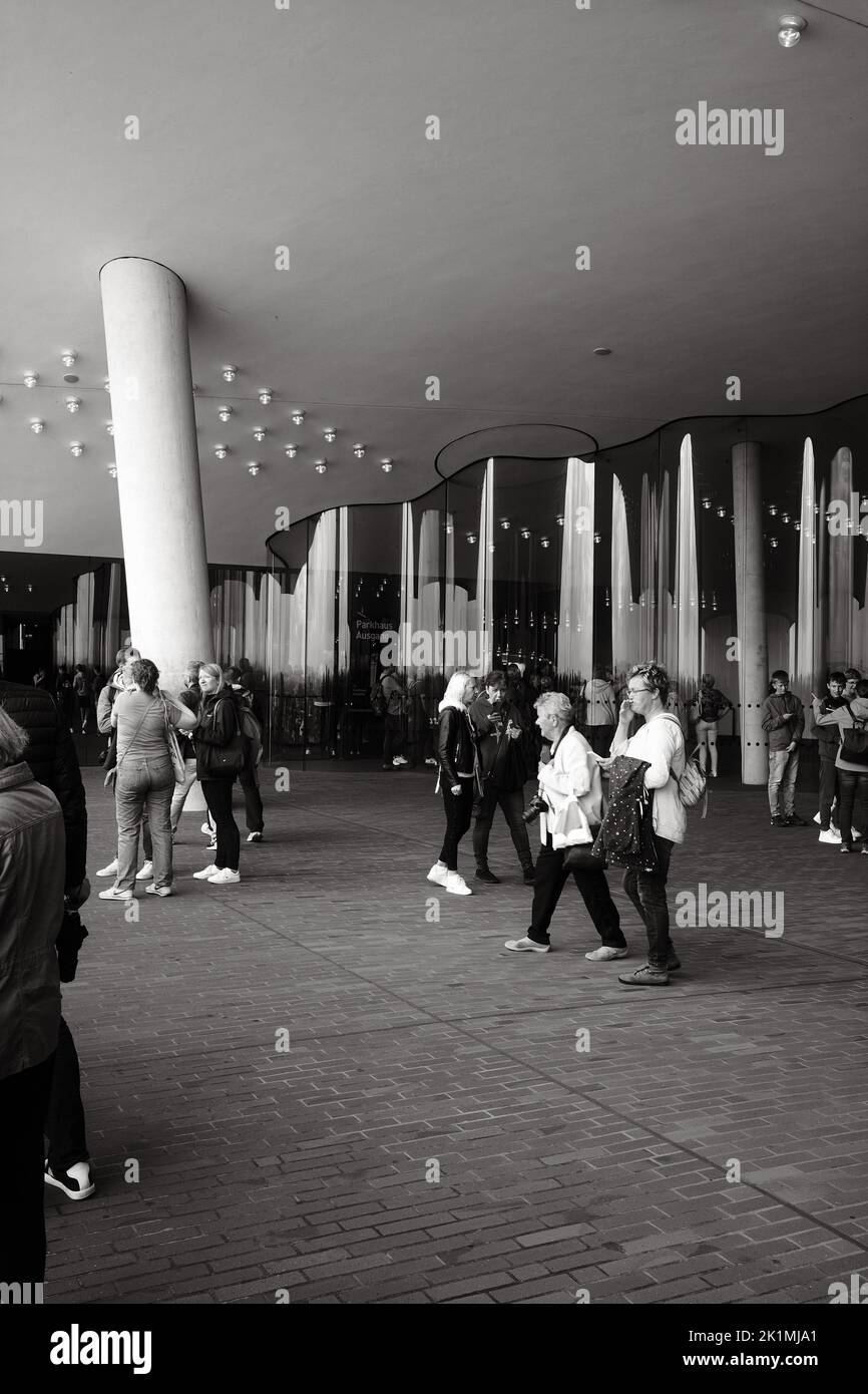 The vertical grayscale view of people walking before the wavy metal facade Stock Photo