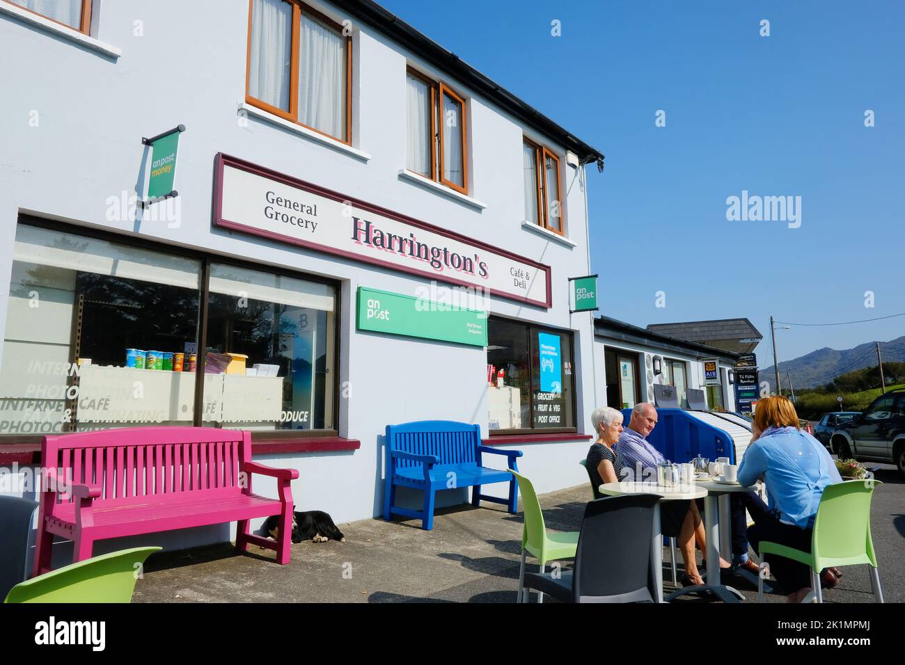 Tourists enjoying a drink outside Ardgroom stores, County Cork, Ireland - John Gollop Stock Photo