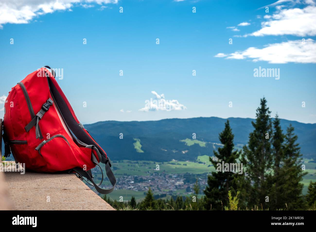 Red backpack or rucksack on a rock with scenic panoramic view of mountain valley and blue sky background as backpacking, travelling journey concept Stock Photo