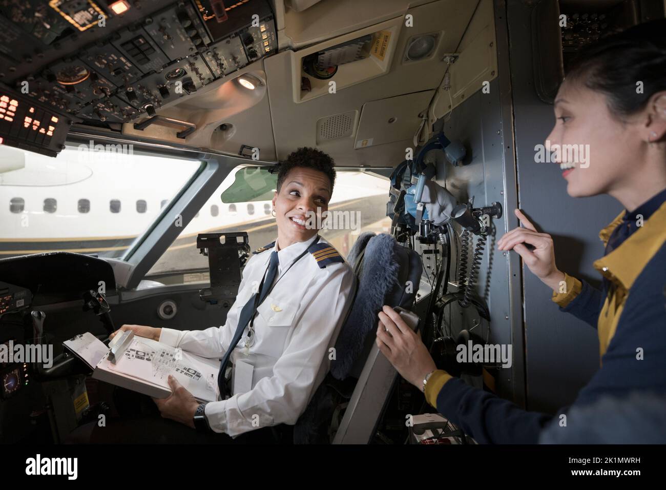 Female flight attendant talking with pilot in airplane cockpit Stock